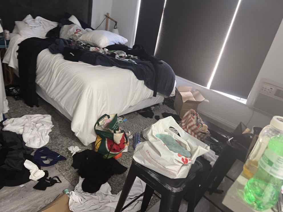 A bedroom full of scattered clothing and rubbish before cleaning began